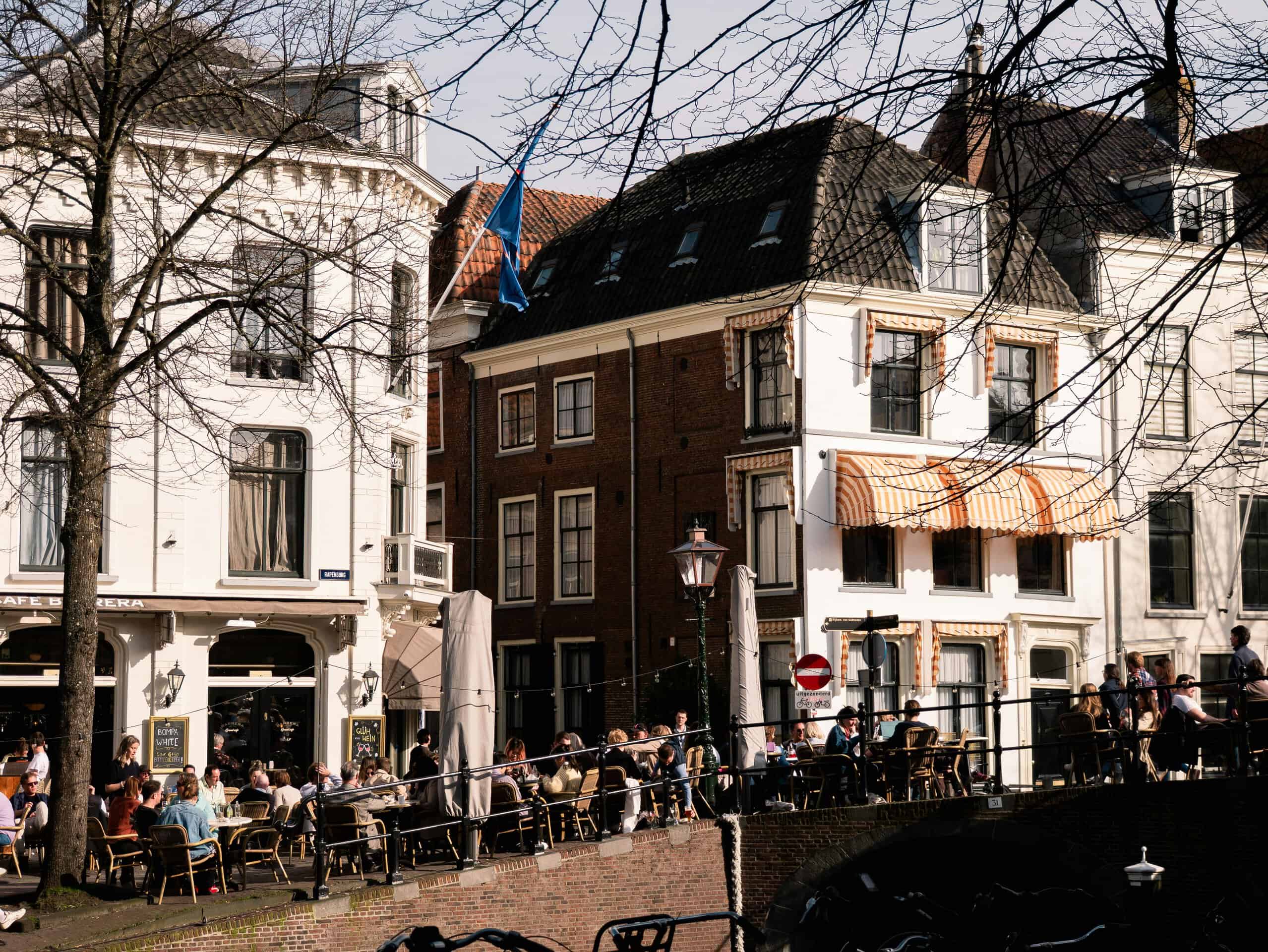 A bustling outdoor cafe in Leiden with people enjoying sunny weather by the canal.