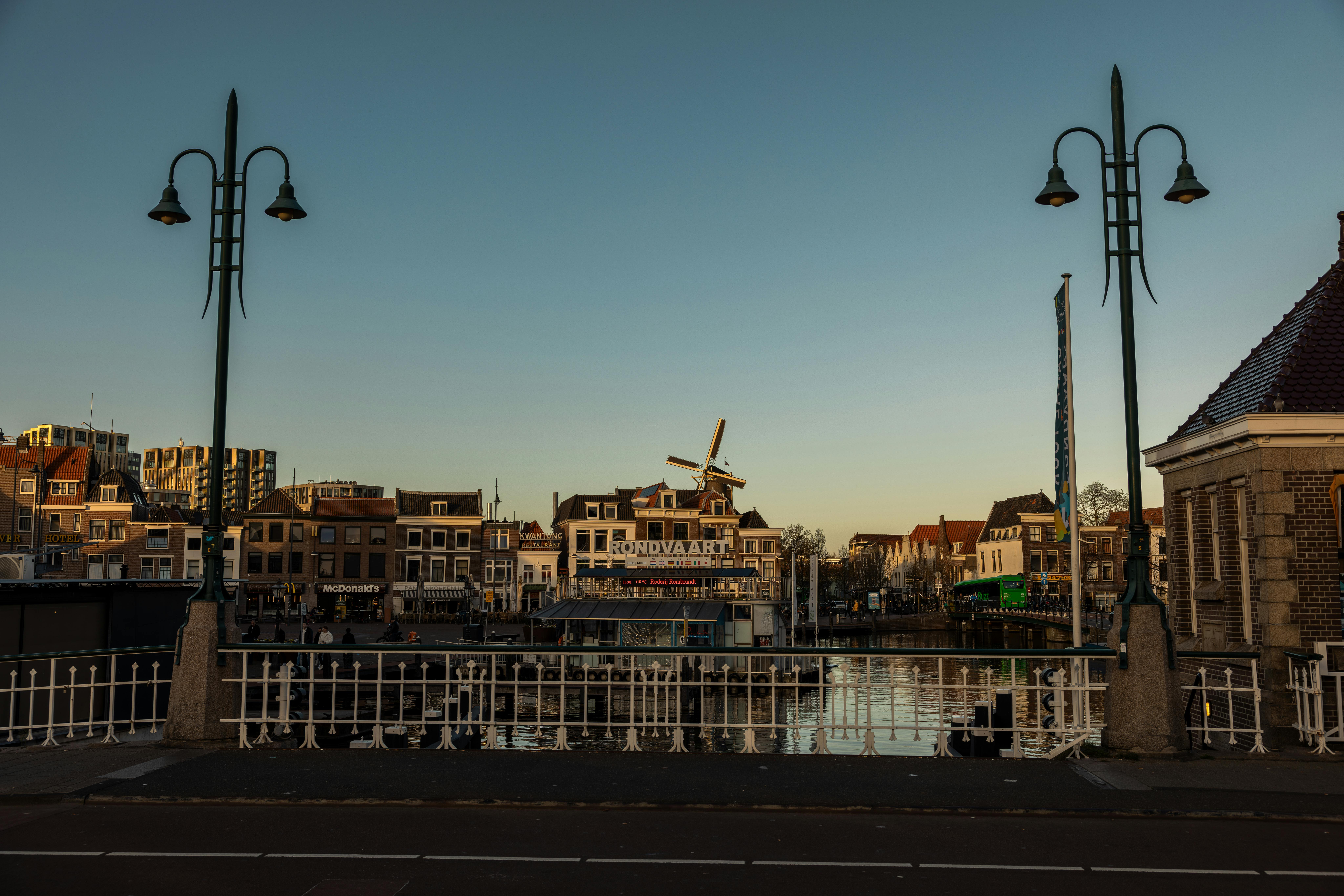 Picturesque Leiden cityscape with canal, bridge, and windmill at twilight. Historic Dutch architecture under a clear sky.